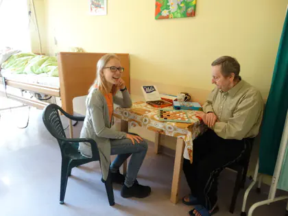 Wolontariuszka w okularach gra w warcaby z mieszkańcem przy stoliku w pokoju
