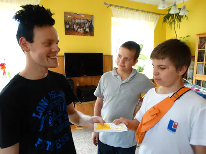 Młodzieniec wręcza kartkę dwóm chłopcom w pokoju wypoczynkowym