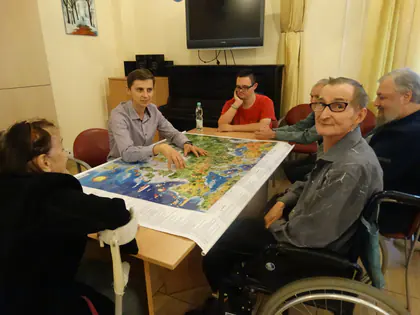Mieszkańcy i wolontariusz siedzą przy stole z kolorową mapą Europy