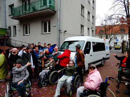 Mieszkańcy machają przy nowym białym samochodzie przystosowanym do przewozu wózków