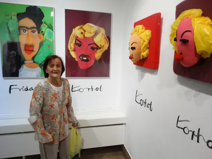 Mieszkanka w kwiecistej bluzce pozuje przy karykaturach z podpisami Frida i Warhol