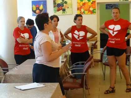 Wolontariusze Coca-Coli w czerwonych koszulkach rozmawiają z pracownicą w świetlicy