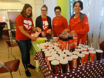 Wolontariuszki w czerwonych koszulkach przy stole z kubkami napojów przed seansem