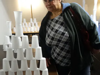 Mieszkanka przygląda się piramidzie z białych plastikowych kubeczków ułożonej na stole