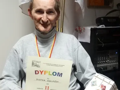 Mieszkaniec na wózku z medalem trzyma dyplom za drugie miejsce i nagrodę