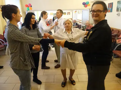 Mieszkańcy i młodzież tańczą trzymając się za ręce w świetlicy z balonami