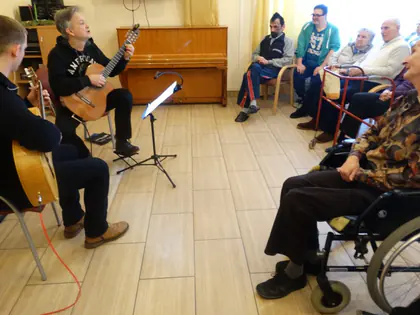 Dwaj gitarzyści grają koncert dla mieszkańców w świetlicy
