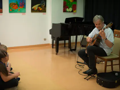 Gitarzysta gra na krześle, dzieci słuchają siedząc na podłodze