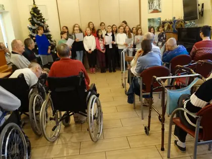 Dzieci kolędują w głębi świetlicy, mieszkańcy słuchają z wózków