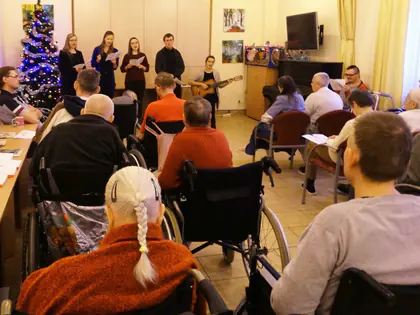 Wolontariusze śpiewają kolędy z gitarą przed mieszkańcami w świetlicy