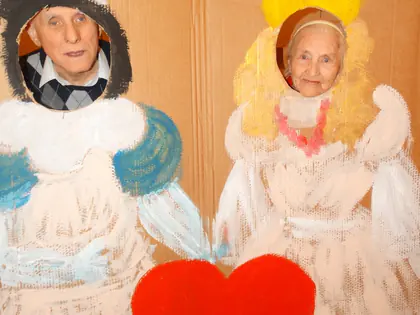 Mieszkaniec i mieszkanka wystawiają twarze przez otwory w malowanej dekoracji z sercem