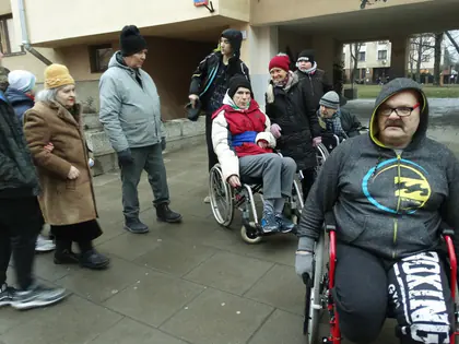 Mieszkańcy na wózkach i młodzież ubrani na zimowy spacer przed budynkiem