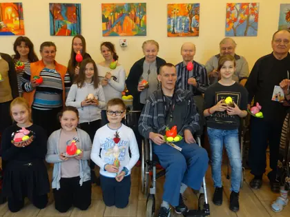 Mieszkańcy i dzieci z wielkanocnymi ozdobami pozują przed kolorowymi obrazami