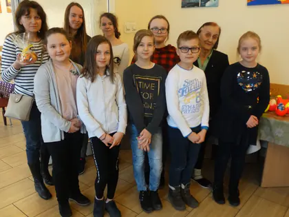 Grupa dzieci, kobiety i starsza mieszkanka pozują razem w świetlicy