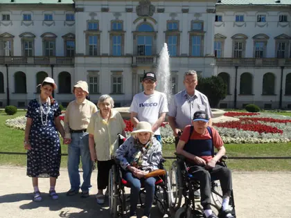 Mieszkańcy z opiekunami przed pałacem z fontanną w Ogrodzie Krasińskich