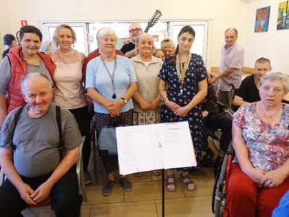 Mieszkańcy i terapeuta z gitarą po koncercie, na pierwszym planie pulpit z tekstem