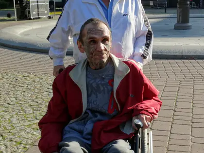 Opiekun prowadzi wózek z mieszkańcem w czerwonej kurtce