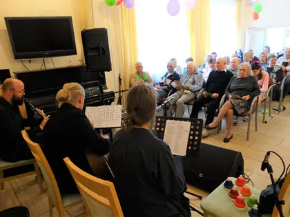 Muzycy grają przed mieszkańcami siedzącymi w rzędach