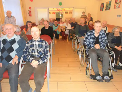 Mieszkańcy siedzą w rzędach, część na wózkach, podczas koncertu