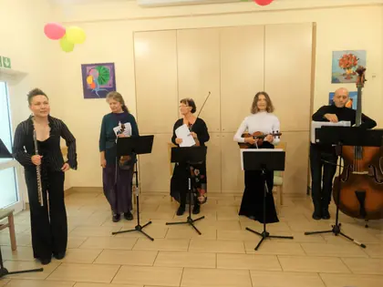Pięcioro muzyków z fletem, skrzypcami i kontrabasem stoi przy pulpitach