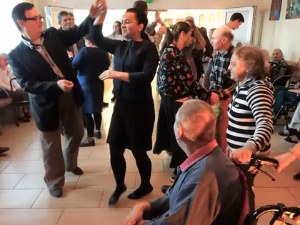 Pary tańczą w świetlicy podczas andrzejek, obok mieszkaniec na wózku