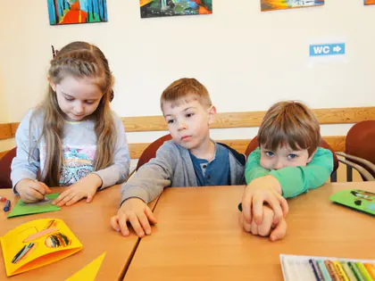 Troje przedszkolaków robi kartki przy stole