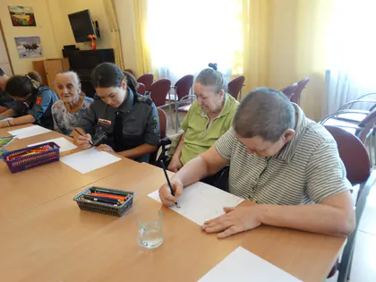 Harcerki i mieszkańcy przy stole piszą i rysują na kartkach