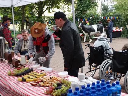 Stół z owocami i napojami, przy nim goście i mieszkańcy