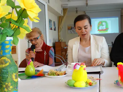 Mieszkanka czyta do mikrofonu przy stole z dekoracjami wielkanocnymi