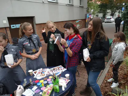 Harcerki z pomalowanymi twarzami przy stoliku z farbami