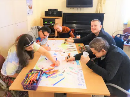 Mieszkańcy rysują kolorowymi pisakami na dużym arkuszu papieru