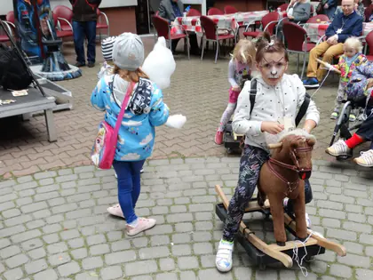 Dziewczynka z pomalowaną twarzą siedzi na drewnianym koniku na biegunach