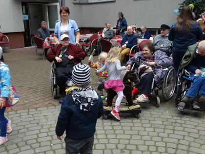 Dzieci bawią się wśród mieszkańców na wózkach przy stołach