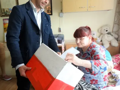 Mieszkanka w łóżku wrzuca kartę do urny podczas wyborów do Rady