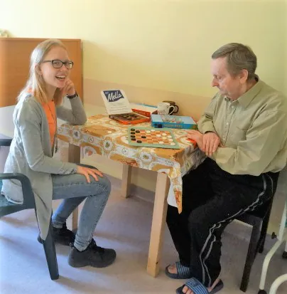 Młoda wolontariuszka gra w warcaby z mieszkańcem przy stoliku.