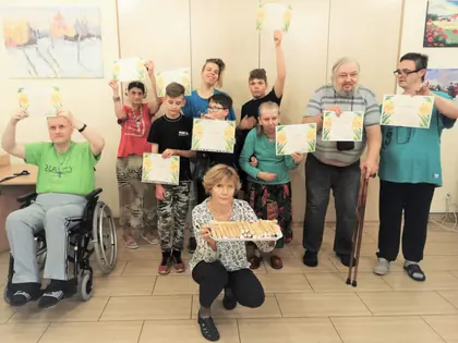 Mieszkańcy i młodzież z dyplomami, na pierwszym planie taca ze słodyczami