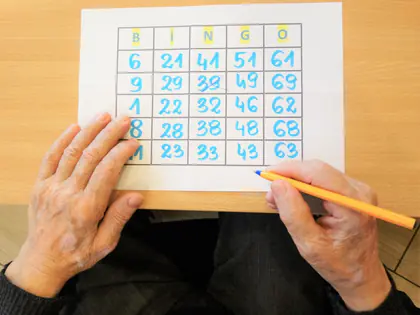 Dłonie trzymają kartę do bingo z niebieskimi liczbami i ołówek