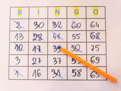 Karta do bingo z liczbami, część skreślona, obok pomarańczowy długopis