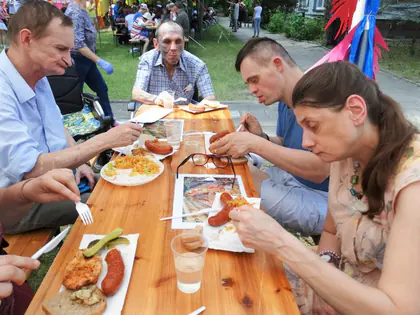 Mieszkańcy jedzą kiełbaski przy drewnianym stole na pikniku
