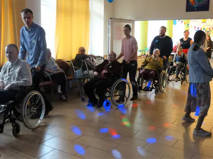 Opiekunowie tańczą z mieszkańcami na wózkach w świetle dyskotekowych kul