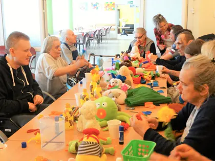 Mieszkańcy robią kwiaty z bibuły przy stole pełnym maskotek