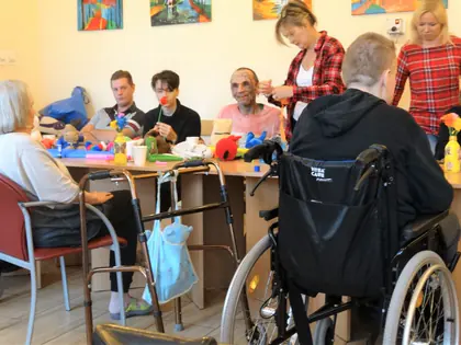 Mieszkańcy i opiekunki przy stole z kolorowymi kwiatami z bibuły