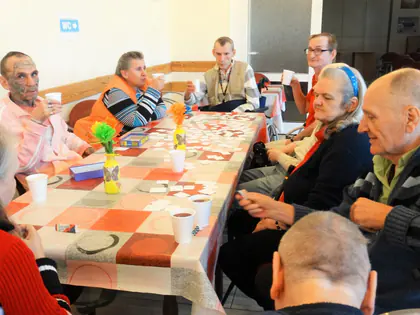 Mieszkańcy przy stołach z kubkami i karteczkami podczas zajęć