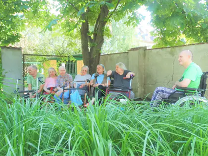 Mieszkańcy siedzą w ogrodzie pod drzewem przy murze
