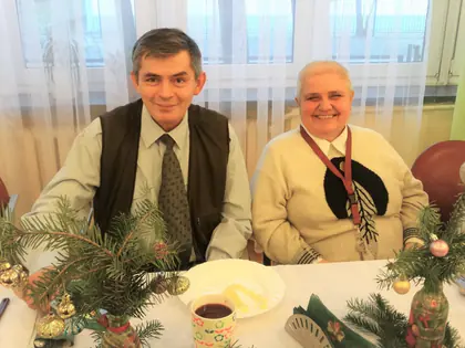 Mieszkaniec i mieszkanka uśmiechają się przy wigilijnym stole ze stroikiem