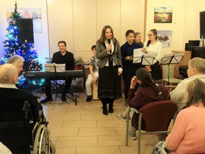 Wokalistka z mikrofonem śpiewa przed mieszkańcami, w tle zespół i choinka