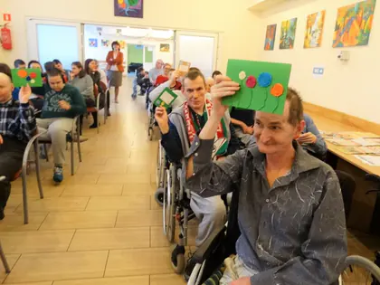 Mieszkaniec podnosi kartkę z kolorowymi kółkami, wokół inni uczestnicy