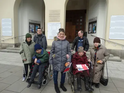 Mieszkańcy, część na wózkach, pozują przed wejściem do kościoła