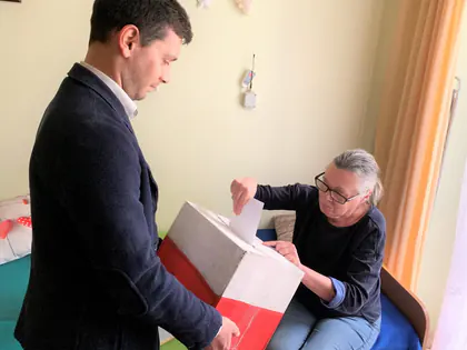 Mieszkanka siedząca na łóżku wrzuca kartę do urny