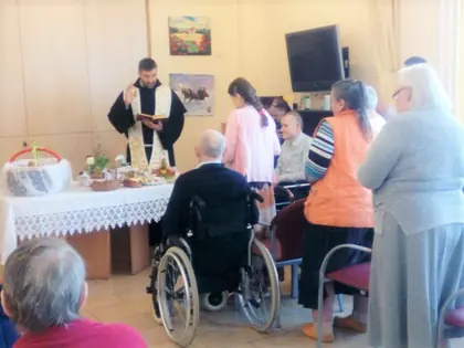 Kapłan święci pokarmy w koszyczkach przy stole, obok mieszkańcy